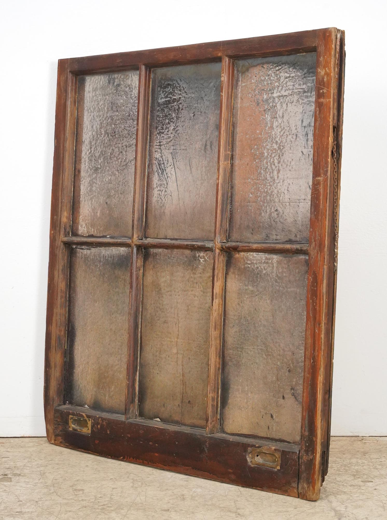 A reclaimed window mirror with six panes in a dark wood frame, showing worn silvered glass and original brass hinges at the bottom.