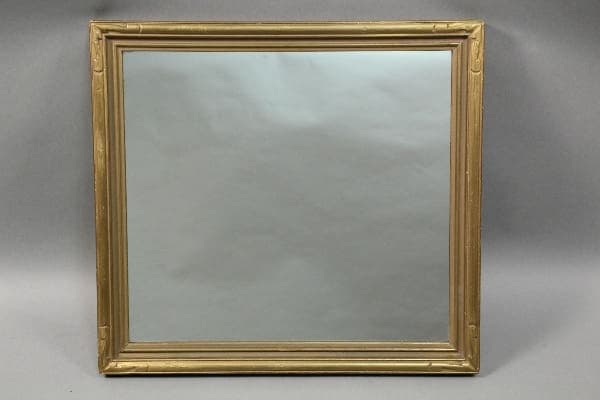 An ornate 10622. Large Scale 1920's mirror against a plain gray backdrop, reflecting a hazy, obscured image.