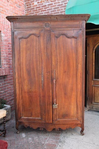 12904. 19th Century Tall French Armoire standing on a brick patio, featuring ornately carved doors and a wavy bottom edge.