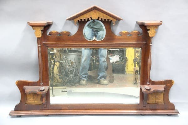 Antique 12989. Turn Of The Century Mirror with inlay and original bevel mirror mantel clock with a reflective glass front that shows a reflection of someone's legs and cluttered background.