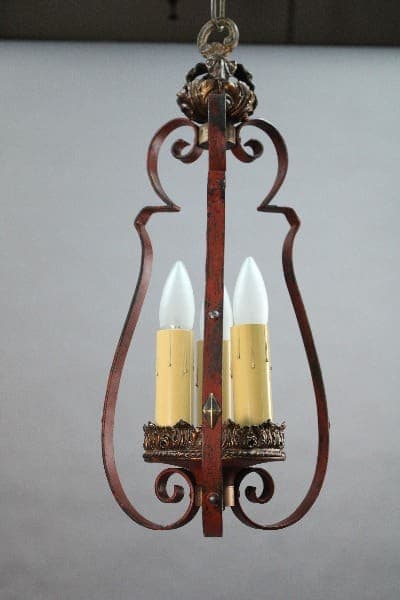 A vintage 15006 Spanish Revival pendant with three lights and a rusty iron frame and cream-colored faux candle covers.