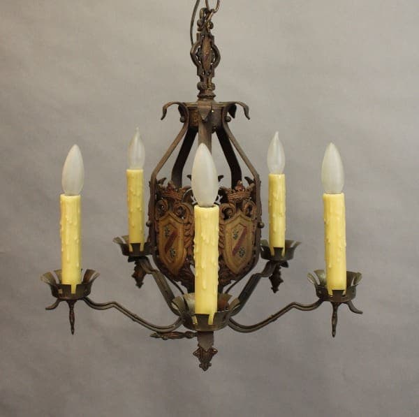 15396. 1 of 2 Spanish Revival Chandelier With Shield Motif with six candle-shaped bulbs and ornate metal designs, suspended from a chain against a neutral background.