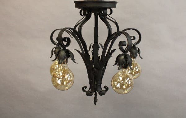 Spanish Revival chandelier with ornate floral designs, featuring four illuminated, clear glass bulbs.