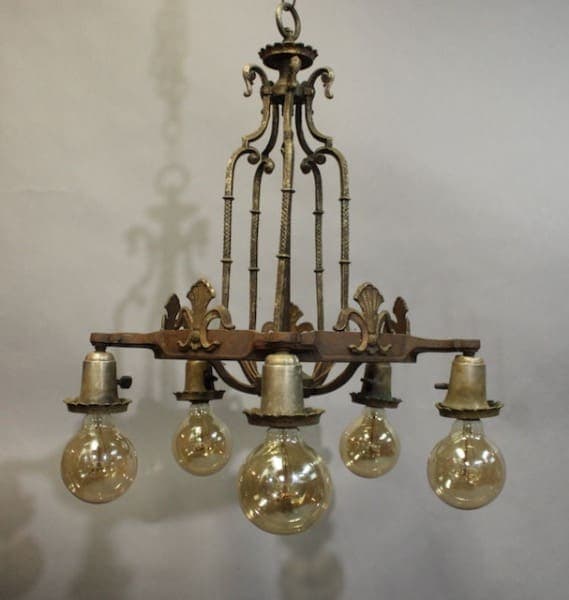 15957. Tudor Style 1920's Chandelier with ornamental designs and five hanging glass bulbs, suspended in a room with a gray background.