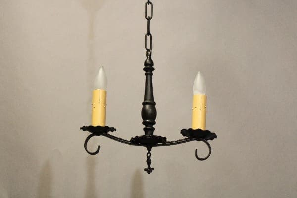 A hanging 16207. Small Spanish Revival 1920's Pendant with a dark metallic finish and two candle-like bulbs against a plain light background.