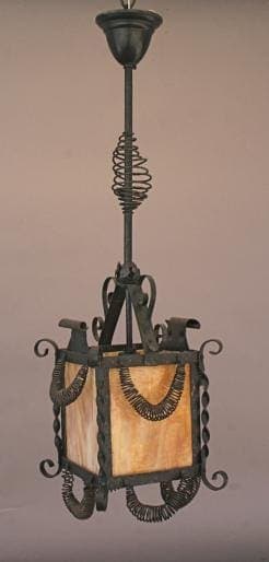 4748. Wrought iron lantern with spiral details and amber glass panels hanging from the ceiling.
