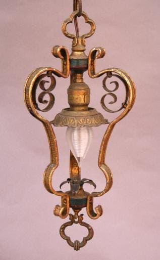 960. Spanish Revival hall pendant with ornate metal scrollwork and a single frosted glass bulb, suspended against a pink background.