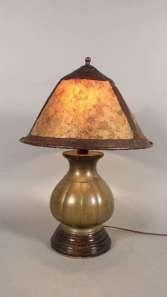An arts and crafts table lamp with bronze Japanese base and mica shade, illuminated, on a neutral background.