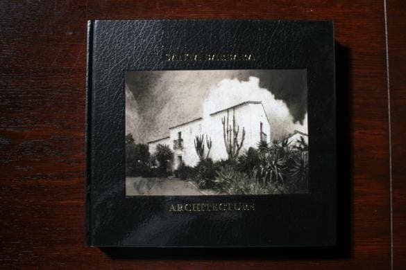 A black hardcover book titled "1293. Santa Barbara Architecture: from Spanish Colonial to Modern" with an embossed photograph of a building surrounded by plants on a wooden surface.
