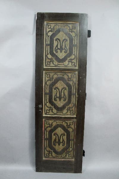 13991. Narrow Spanish Revival 1920's Pantry Door with ornate metal panels featuring symmetrical decorative motifs, positioned upright against a plain background.