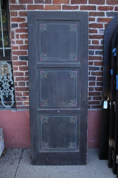 An upright 14776. Spanish Revival 1920's door with four panels, each adorned with a simple floral design, leaning against a red brick wall.