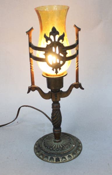 14997. Antique electric table lamp with ornate metal details, illuminated yellow glass shade, and a turned wooden base, on a white background.