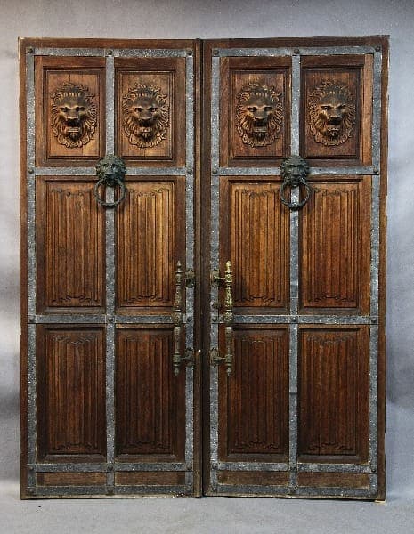 15346. Stately Turn Of the Century Pair of Palatial Doors With Linen Fold and Lion Carvings with metal ring knockers, set against a gray backdrop.