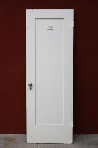 A 6551. 1920s Single Panel Interior Door CC with a silver handle, standing upright against a red wall.