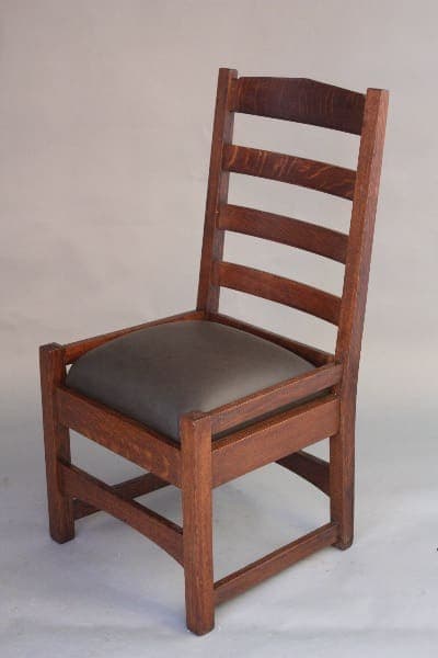 8455. Arts And Crafts Oak Ladder Back Chair with a dark brown finish and a padded, black leather seat cushion, against a neutral gray background.