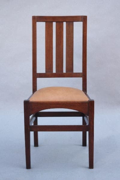A 9807. 1910 Arts & Crafts Side Chair featuring a tall, vertical slat back design and a light beige cushioned seat, set against a plain gray background.