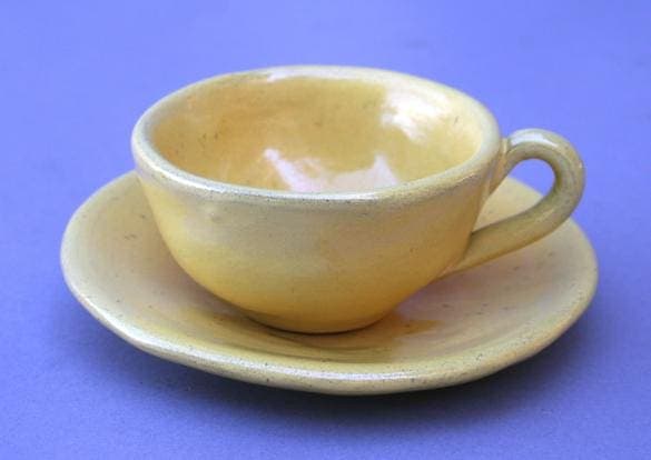 Yellow ceramic cup and saucer on purple background.