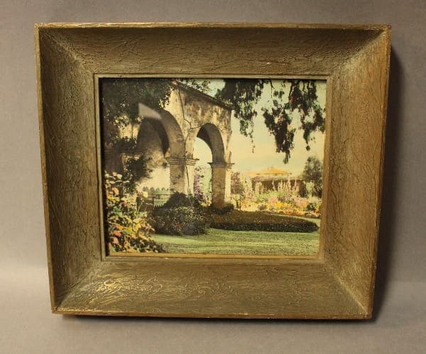 Framed painting of an arch and garden.